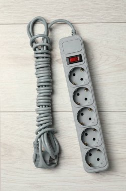 Beyaz ahşap zemin üzerinde uzatma kablosu olan güç şeridi, üst manzara. Elektrikçi ekipmanı.