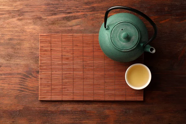 Bamboo mat, teapot and cup of tea on wooden table, top view. Space for text