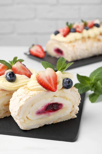 stock image Pieces of tasty meringue roll with jam, cream, strawberry, blueberry and mint on white table