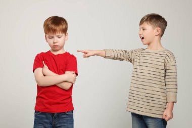 Boy laughing and pointing at upset kid on light grey background. Children's bullying clipart