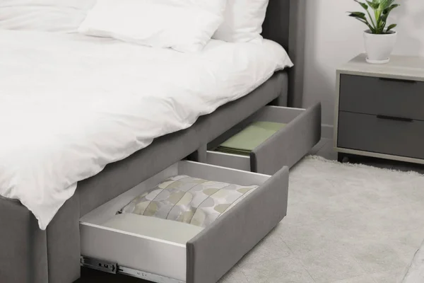 Storage drawers with bedding under modern bed in room. Space for text