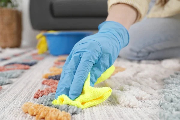 Woman in rubber gloves cleaning carpet with rag indoors, closeup