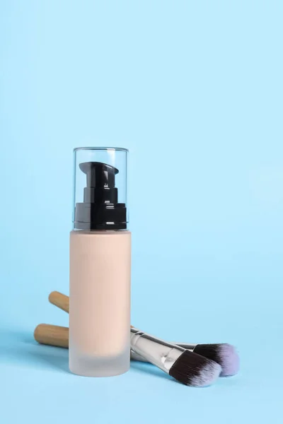 Bottle of skin foundation and brushes on light blue background. Makeup product