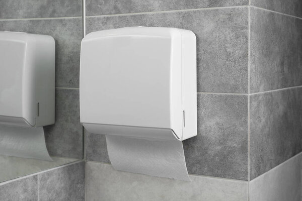 New paper towel dispenser hanging on wall near mirror in bathroom