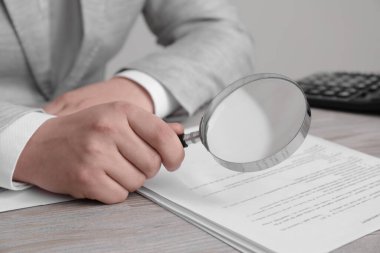 Beyaz ahşap masaya büyüteçle bakan bir adam, yakın plan. Konsept aranıyor