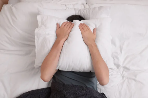 Man covering his face with pillow in bed, top view