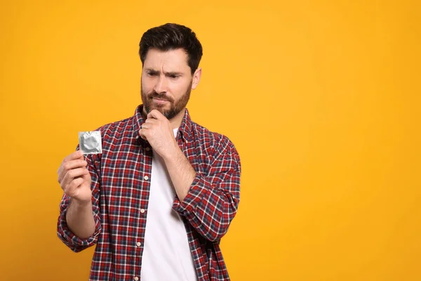 Confused Man Holding Condom Yellow Background Space Text Safe Sex — Stock Photo, Image