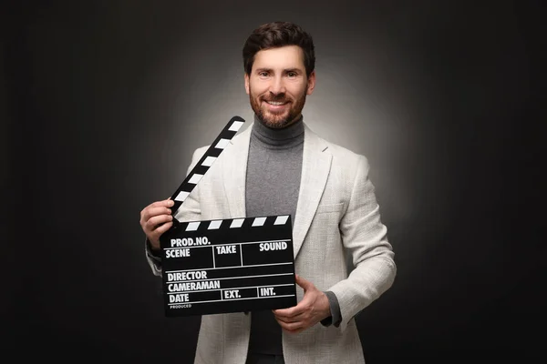 Smiling actor holding clapperboard on black background