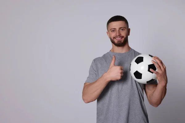軽い灰色の背景に親指を示すサッカーボールを持つ陸上競技の若い男 テキストのスペース — ストック写真