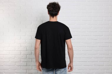 Beyaz tuğla duvarın yanında siyah tişört giyen bir adam. Tasarım için model