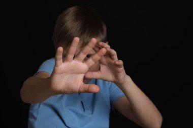 Boy making stop gesture against black background, focus on hands. Children's bullying clipart