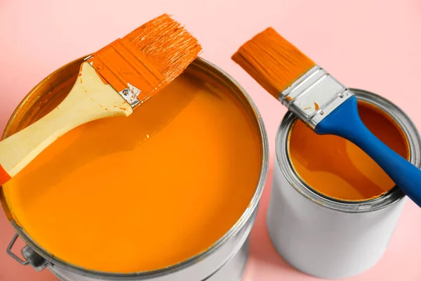 Bucket of orange paint, can and brushes on pink background, closeup