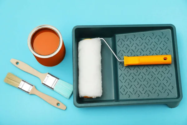 Can of orange paint, brushes, roller and container on turquoise background, flat lay
