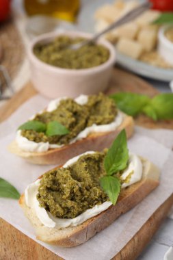 Krem peynirli lezzetli bruschettalar, pesto sosu ve ahşap tahtada taze fesleğen, yakın plan.