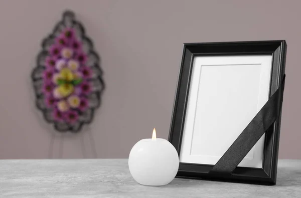黒いリボンで写真フレーム テーブルの上にろうそくを燃焼し 灰色の壁 テキストのためのスペースの近くにプラスチックの花の花輪 葬儀の属性 — ストック写真