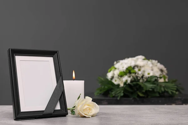 带有黑色缎带的相框 燃烧的蜡烛 玫瑰在明亮的桌子上 花环靠近灰色的墙壁 空间为文字 丧葬属性 — 图库照片