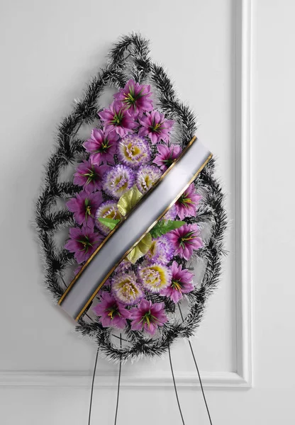Wieniec Pogrzebowy Plastikowych Kwiatów Wstążką Przy Białej Ścianie — Zdjęcie stockowe