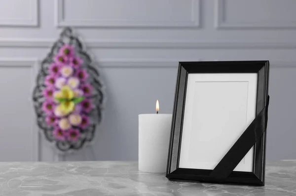 黒いリボンで写真フレーム ライトグレーのテーブルの上にろうそくを燃焼し 壁の近くにプラスチックの花の花輪を屋内で テキストのためのスペース 葬儀の属性 — ストック写真