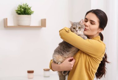 Young woman kissing her adorable cat at home, space for text