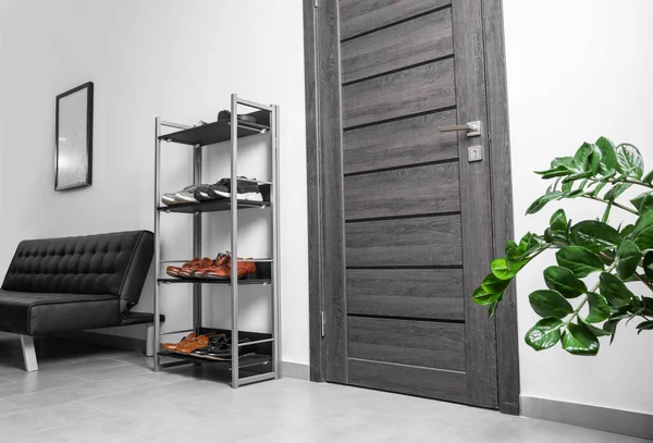 Shoe storage unit and stylish leather sofa near wooden door in hallway. Interior design