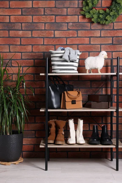 Modern shoe storage bench and potted plant near red brick wall in hallway. Interior design