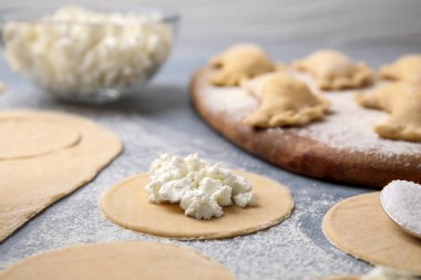 Süzme peynirli hamur tatlısı (varenyky) yapma süreci. Çiğ hamur ve malzemeler gri masada, yakın plan.