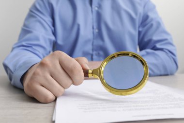 Beyaz ahşap masaya büyüteçle bakan bir adam, yakın plan. Konsept aranıyor