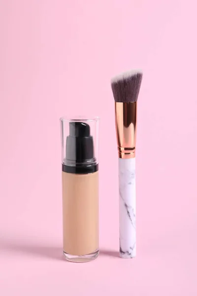 Bottle of skin foundation and brush on pink background. Makeup product