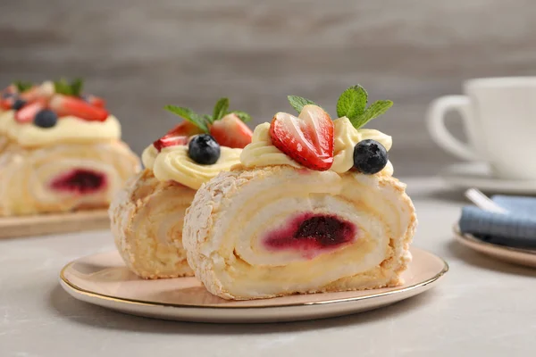 stock image Pieces of tasty meringue roll with jam, cream, strawberry, blueberry and mint on light grey marble table, closeup