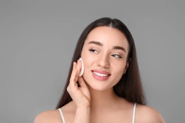 Gri arka planda pamuklu ped ile makyajı kaldıran güzel bir kadın.