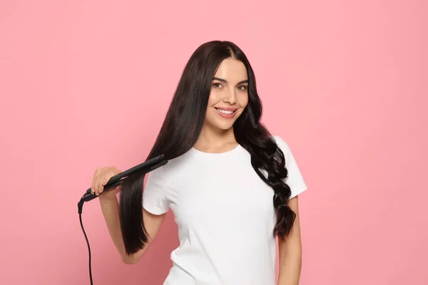 Güzel Mutlu Kadın Pembe Arka Planda Saç Ütüsü Kullanıyor — Stok fotoğraf