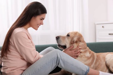 Evdeki kanepede şirin Labrador Retriever 'ı olan mutlu kadın.