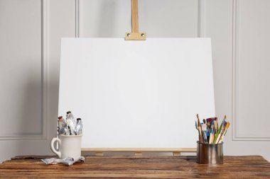 Beyaz duvarın yanındaki ahşap masada boş tuval ve farklı sanat malzemeleriyle.