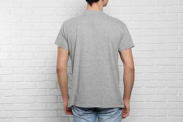 Man wearing gray t-shirt near white brick wall, back view. Mockup for design