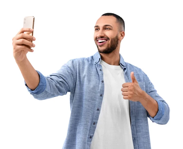 笑着拿着智能手机自拍的年轻人 在白色背景下竖起大拇指 — 图库照片