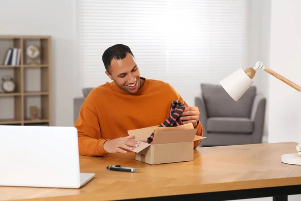 stock image Happy young man opening parcel at table indoors. Internet shopping