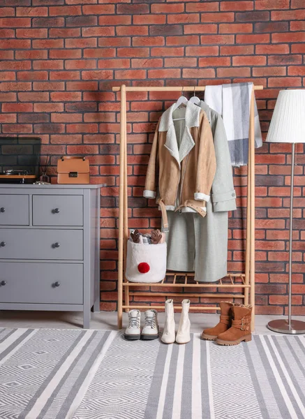 Beautiful hallway interior with coat rack and chest of drawers near red brick wall