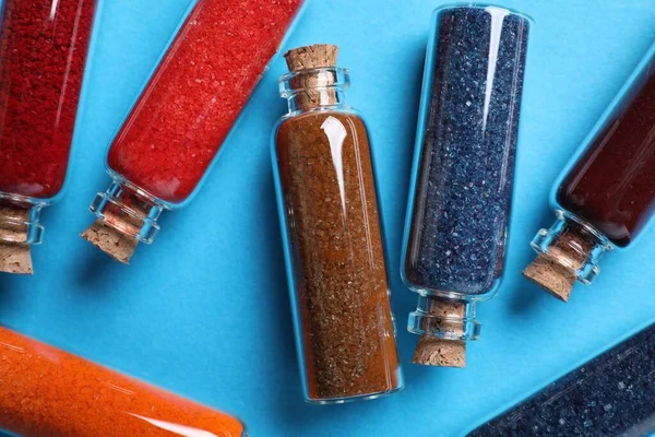 stock image Glass bottles with different food coloring on light blue background, flat lay