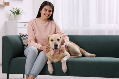 Evdeki kanepede şirin Labrador Retriever 'ı olan mutlu kadın.