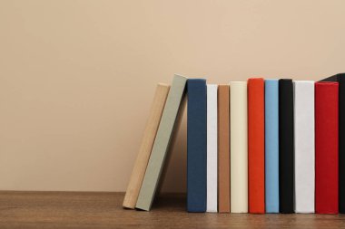 Bej duvarın yakınındaki ahşap masada birçok farklı ciltli kitap var. Metin için boşluk