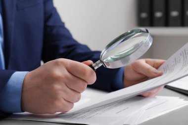 Beyaz masada büyüteçle belgeye bakan adam, yakın plan. Konsept aranıyor