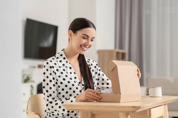 室内のテーブルで幸せな若い女性が小包を開く インターネットショッピング — ストック写真