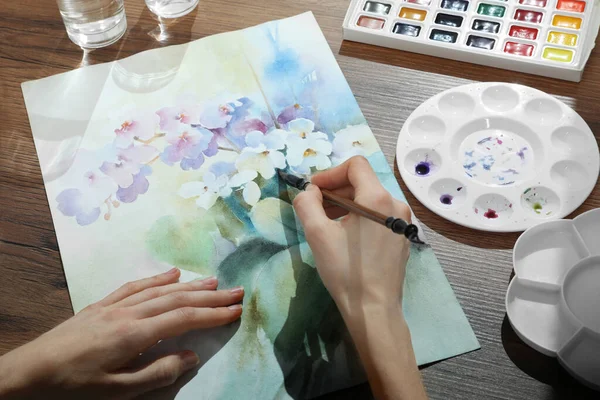 stock image Woman painting flowers with watercolor at wooden table, closeup. Creative artwork