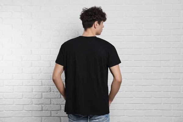 男黒のTシャツを着て白いレンガの壁の近くに バックビュー デザインのためのモックアップ — ストック写真