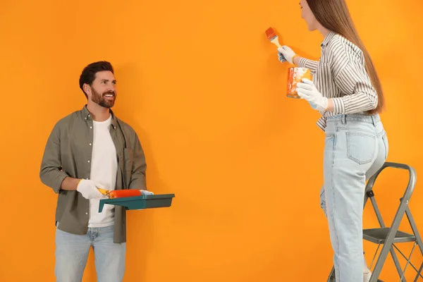 Γυναίκα Ζωγραφική Πορτοκαλί Τοίχο Και Άνθρωπος Κρατώντας Δοχείο Κύλινδρο Εσωτερική — Φωτογραφία Αρχείου