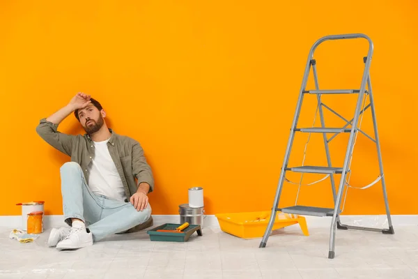 Κουρασμένος Σχεδιαστής Κάθεται Στο Πάτωμα Κοντά Φρεσκοβαμμένο Πορτοκαλί Τοίχο Εσωτερικούς — Φωτογραφία Αρχείου