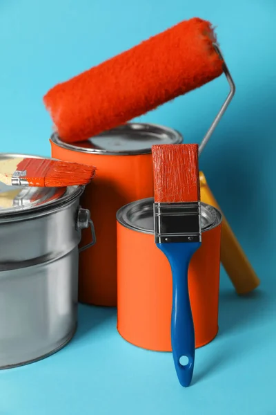 Cans of orange paint, bucket, roller and brushes on turquoise background