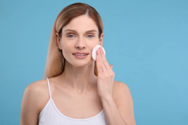 Açık mavi arkaplanda pamuk yastıkla makyajı kaldıran güzel bir kadın.