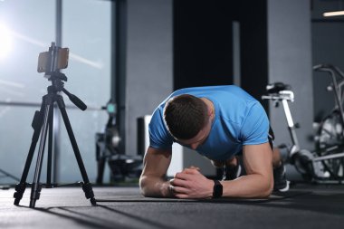 Trainer streaming online workout with phone at gym