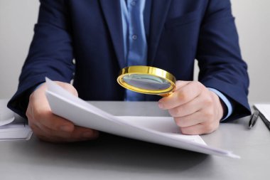 Beyaz masada büyüteçle belgeye bakan adam, yakın plan. Konsept aranıyor